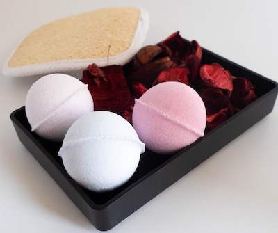 Three aromatherapy bath bombs on a black tray with cloth and loofa.