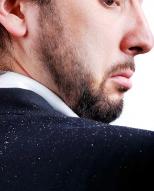 A man looking over his shoulder at the dandruff on his jacket.